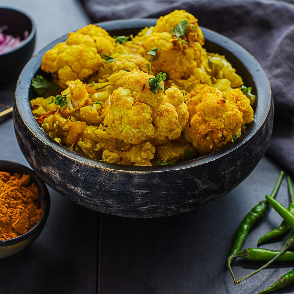 Close-up of Kasa Indian Eatery's Gobi Matar, a vibrant yellow cauliflower and pea curry in a dark bowl.