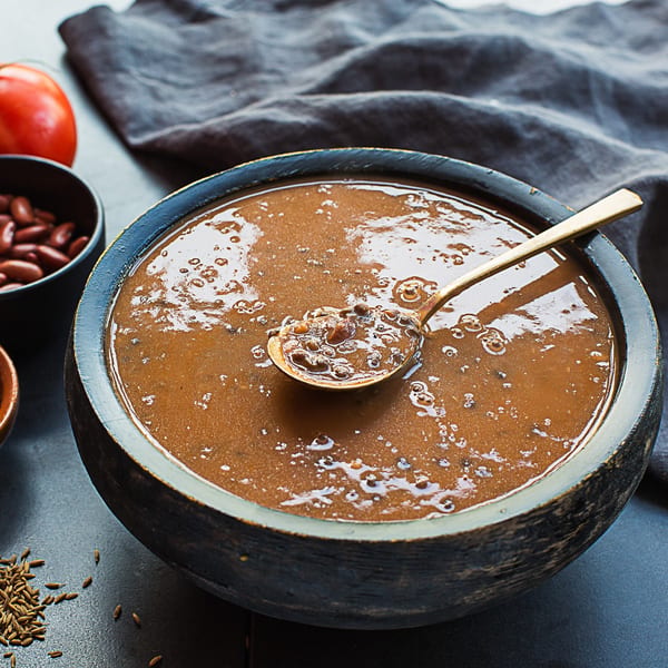 A dark wooden bowl of Kasa Indian Eatery's Dal Makhani, with a gold spoon, beans, and cumin seeds.