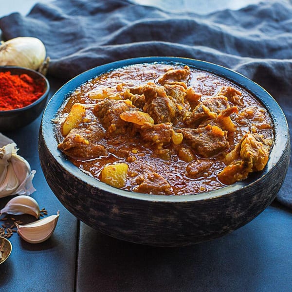 Kasa Indian Eatery's spicy lamb curry in a dark bowl, with garlic, onion, and red spice.