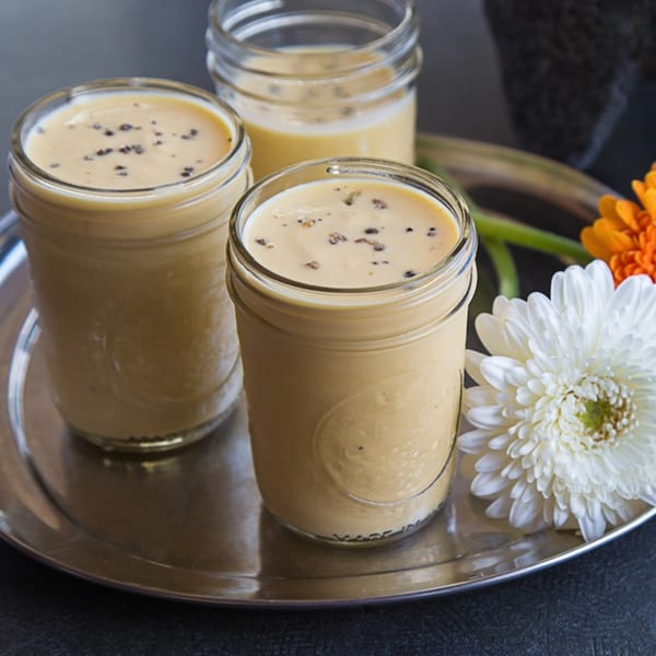 Three glasses of Kasa Indian Eatery's mango lassi, garnished with black pepper, on a silver tray.