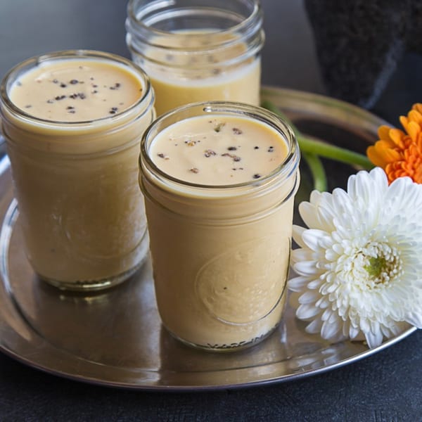 Three glasses of Kasa Indian Eatery's mango lassi on a silver tray with flowers.