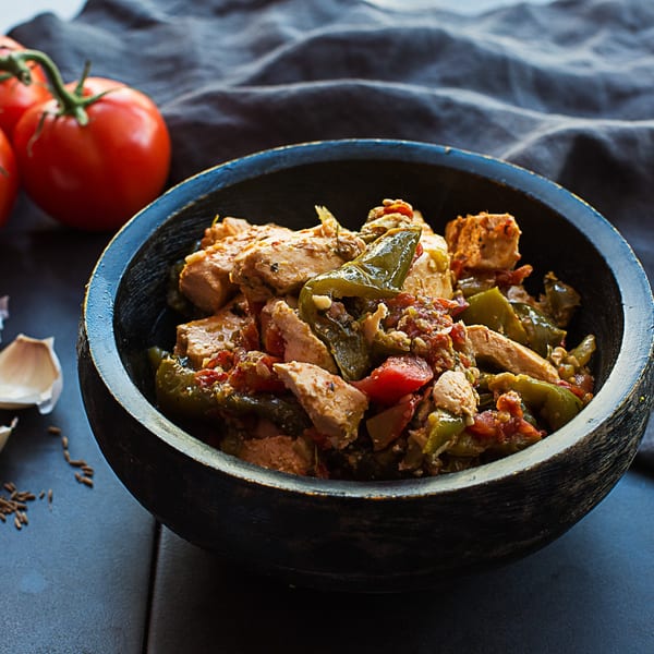 Indian chicken curry with green peppers and tomatoes in a dark wooden bowl.