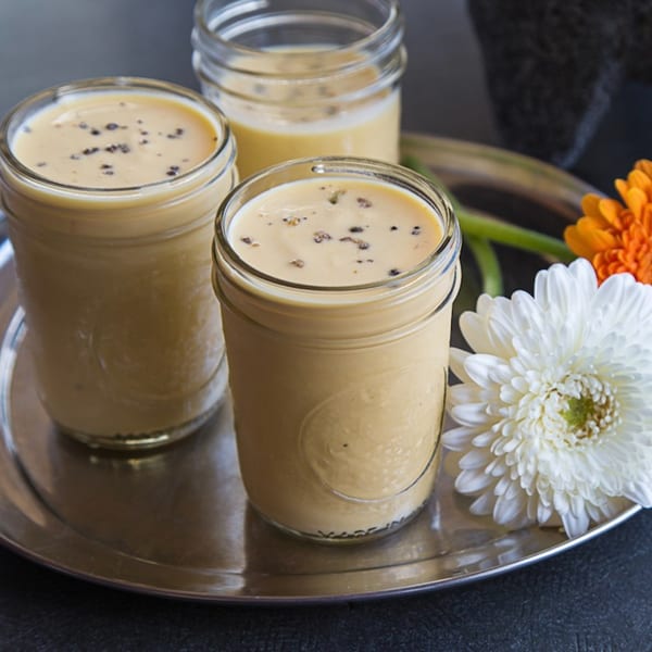 Three glasses of mango lassi with black pepper, garnished with white and orange flowers.