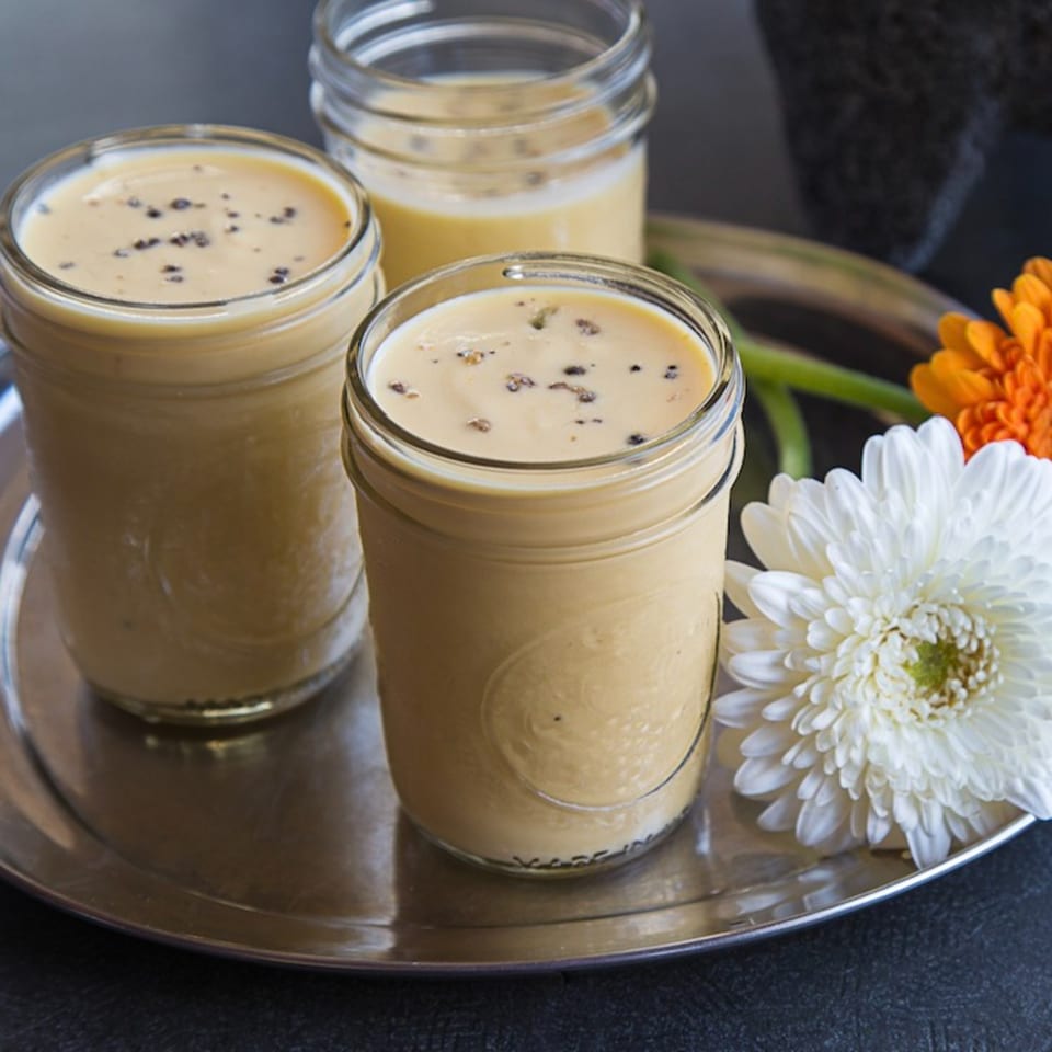Three glasses of mango lassi with black pepper, garnished with white and orange flowers.